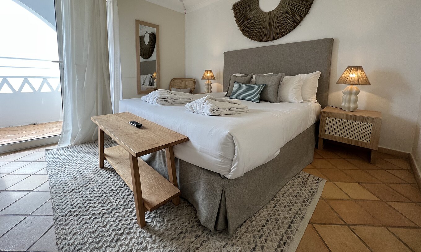 The T2 Apartment Premium do Pestana Palm Gardens has a bed with two bathrobes, cushions and a window with a balcony
