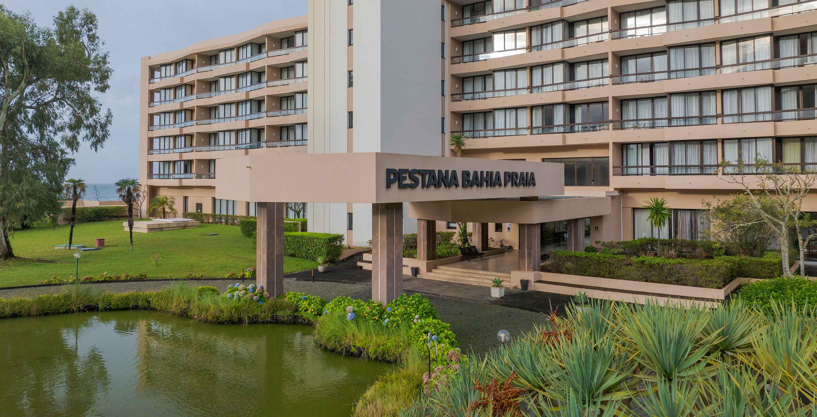 Main entrance of Pestana Bahia Praia with pond, tropical plants, and modern facade in the background