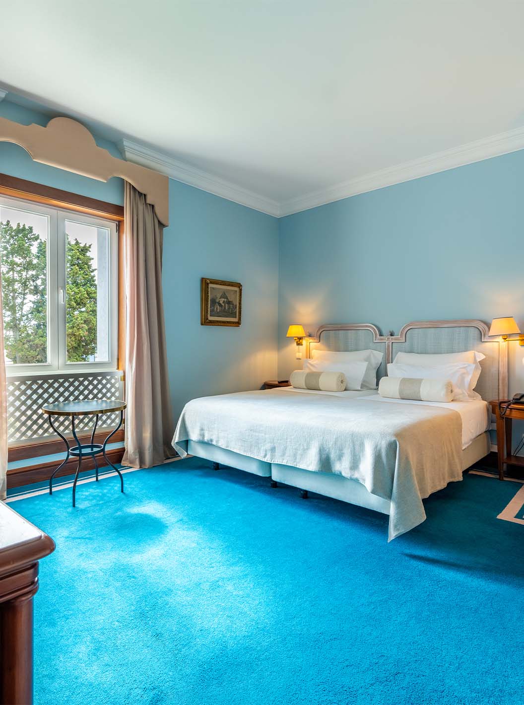 The Deluxe room at Pestana Palace Lisbon has two single beds, a window, an armchair, a desk, and a blue carpet