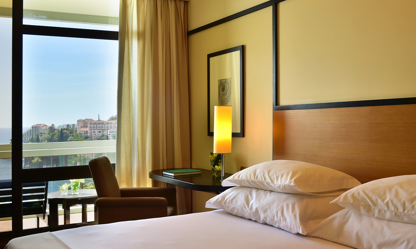 The Classic Side Sea View room at Pestana Casino Park has a double bed, a desk with a lamp, and a balcony