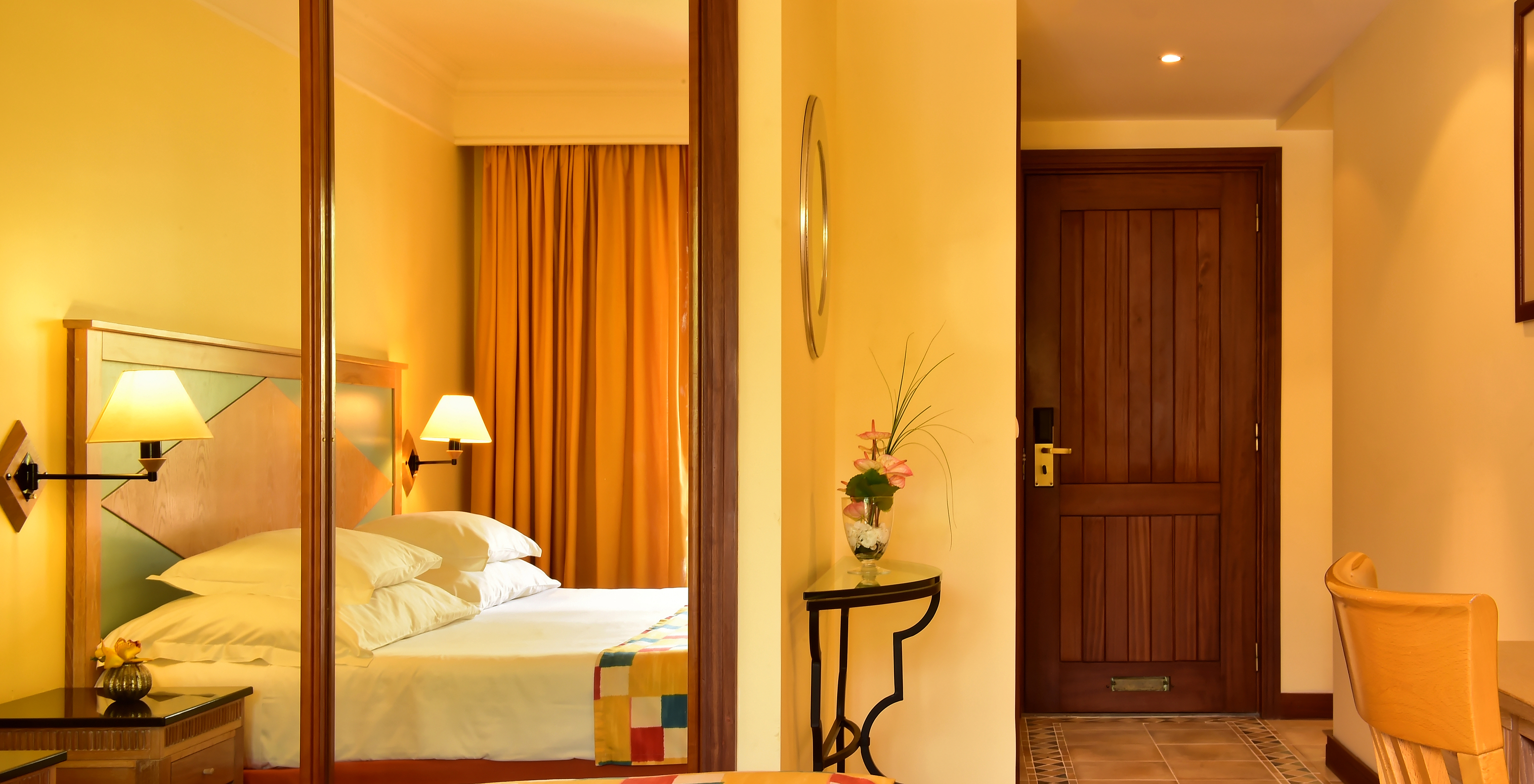 The Superior Room at Pestana Miramar has a double bed with a checkered quilt and a wardrobe with mirror