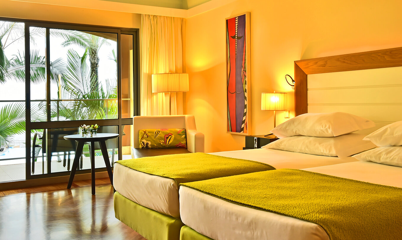 The Classic Pool View of Pestana Promenade has two beds with a green bedspread and a large window to the balcony