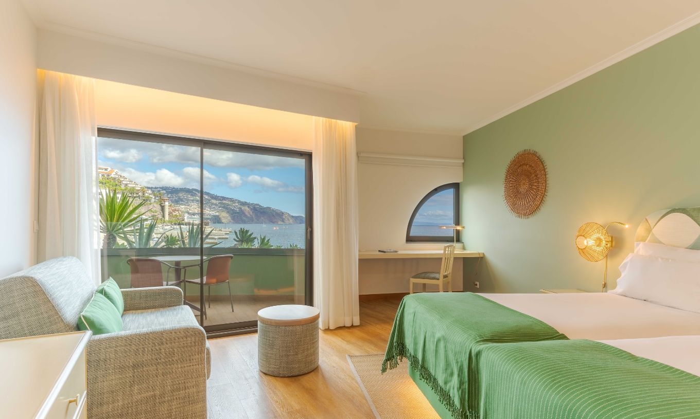 The Superior Side Sea View at the Pestana Vila Lido Madeira has a large window leading out onto the balcony, a desk and a sofa
