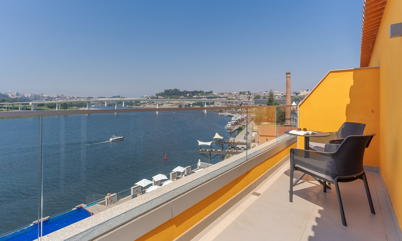 The Junior Suite at Pestana Douro Riverside includes a balcony with a view of the Douro River, and a table with chairs