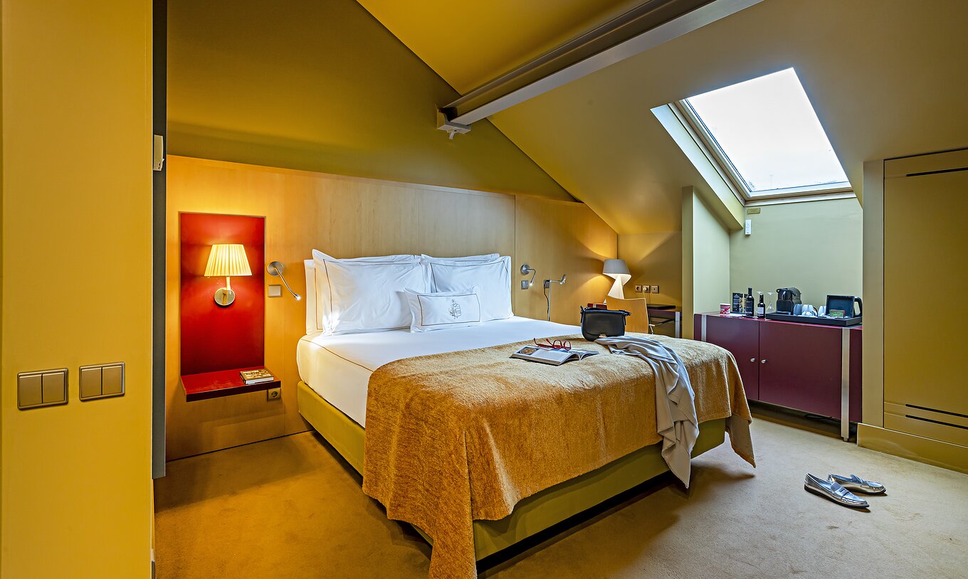 Pestana Palácio do Freixo’s Classic Attic has a bed with a yellow cover and a red bedside table