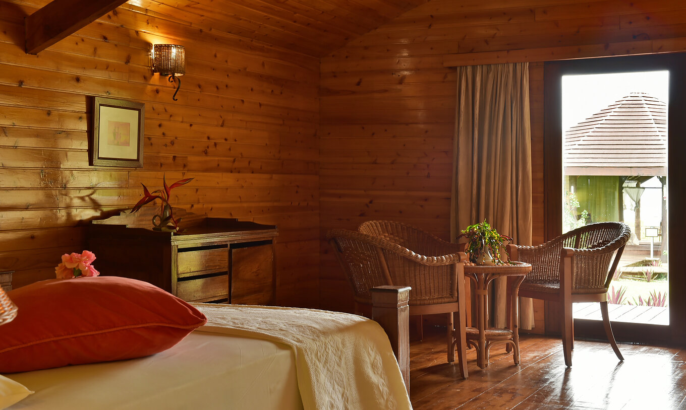 The Superior Double at Pestana Equador Ilheu das Rolas features a bed, a wooden dresser, and a rattan table and chairs