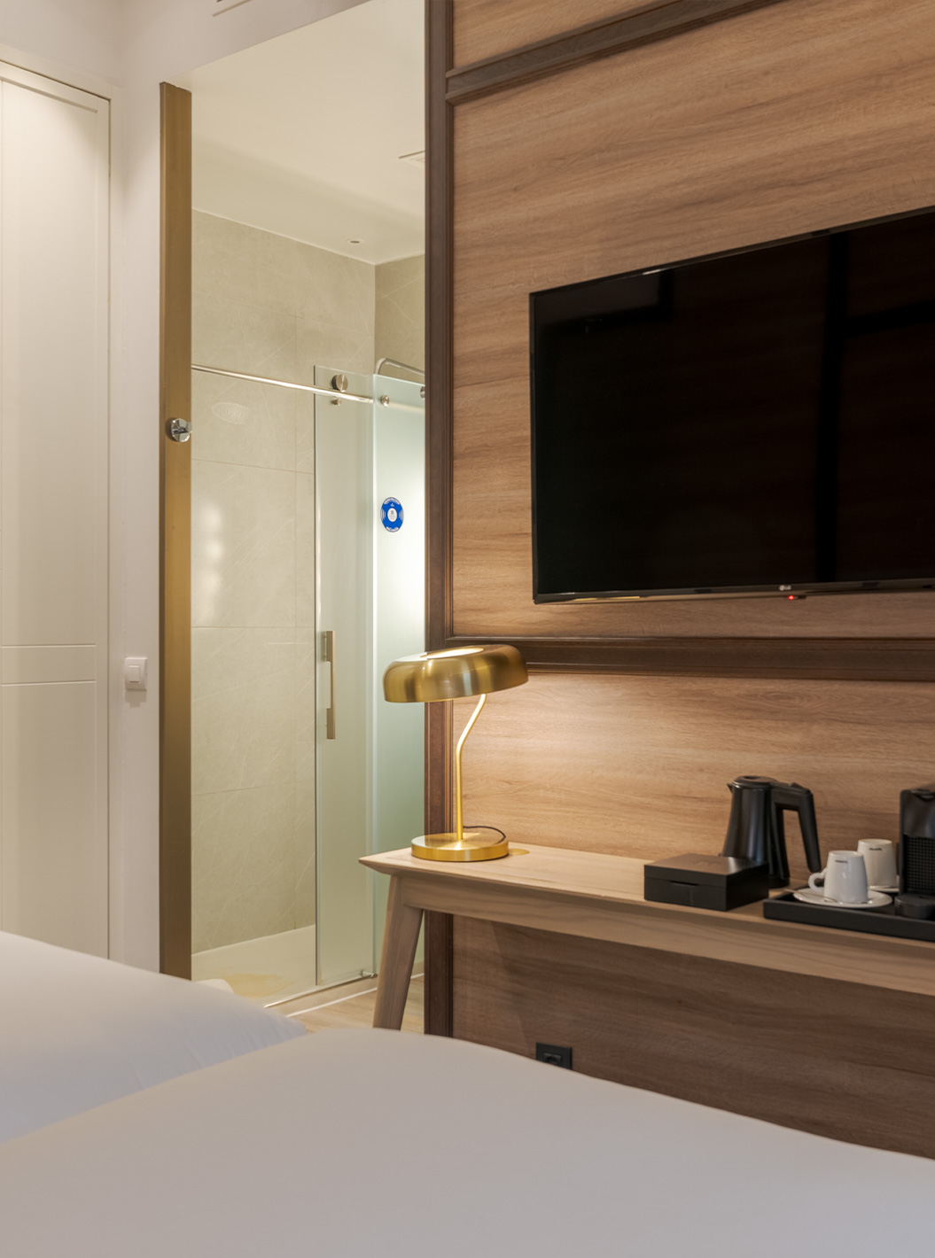 Superior room at Pestana CR7 Gran Vía Madrid featuring wall TV, desk lamp and glass shower area with wood panel décor