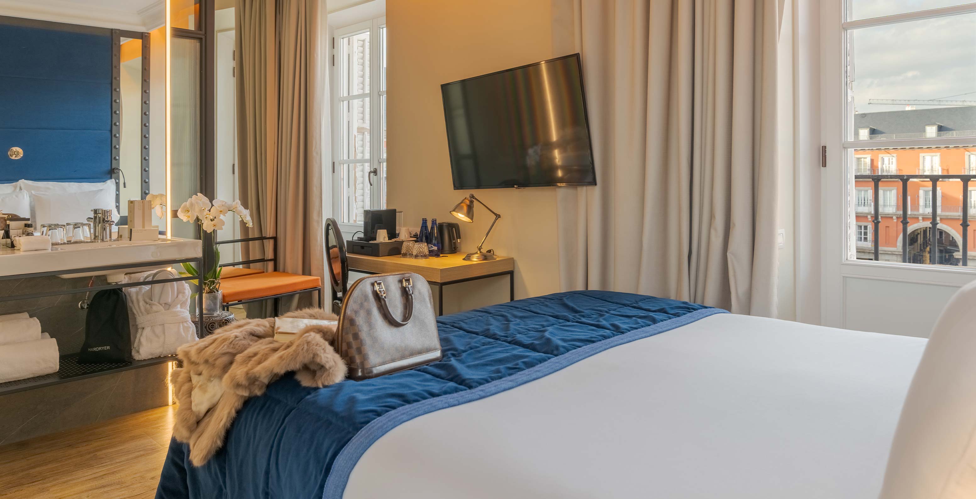 Deluxe Plaza at Pestana Collection Plaza Mayor featuring a blue bed, desk, wall TV and balcony windows