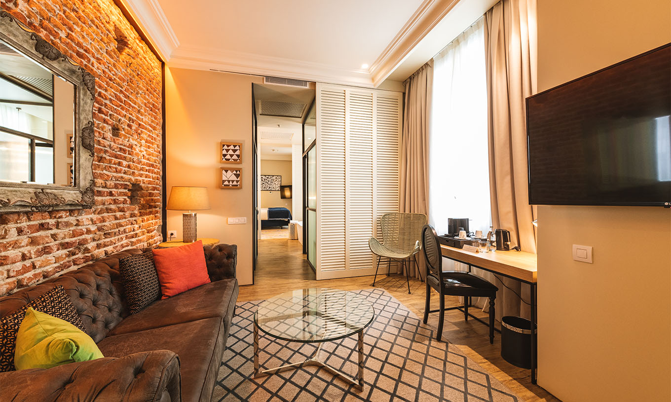 The Suite at Pestana Plaza Mayor Madrid has a living room with desk, sofa, TV and a brick wall