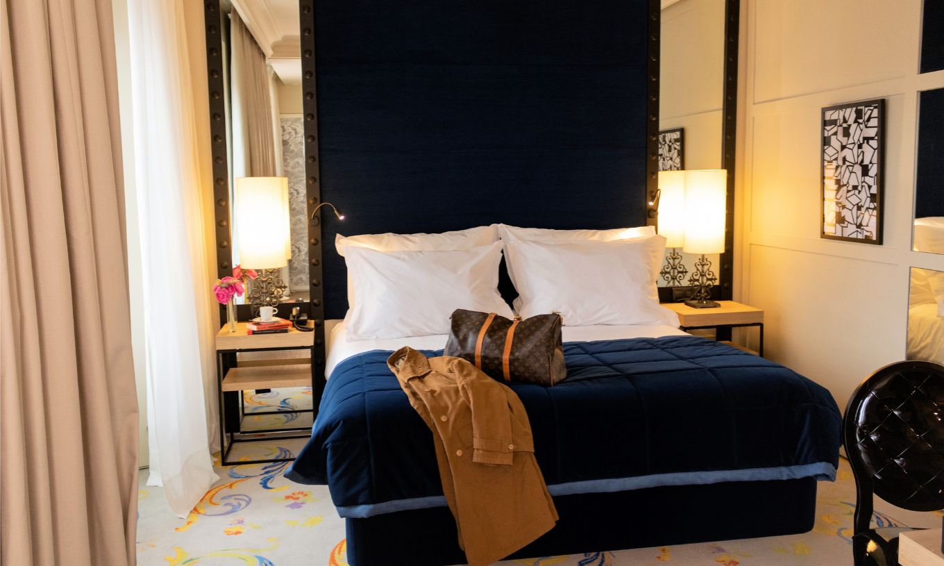 The Superior Plus Room at Pestana Plaza Mayor Madrid has a double bed with a suitcase and a coat on the bed.