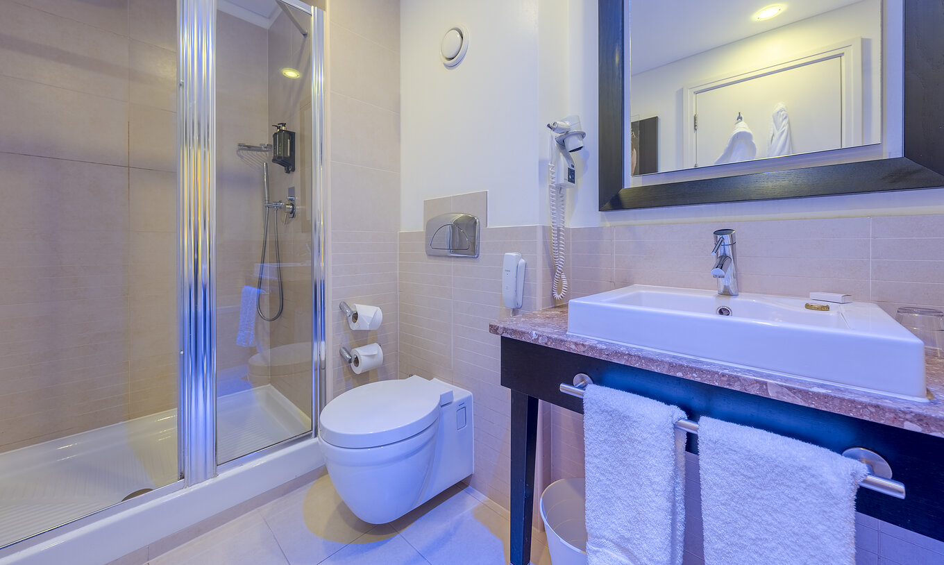 The Superior Twin at Pestana Chelsea Bridge has bathroom with glass-door shower, toilet, sink and mirror