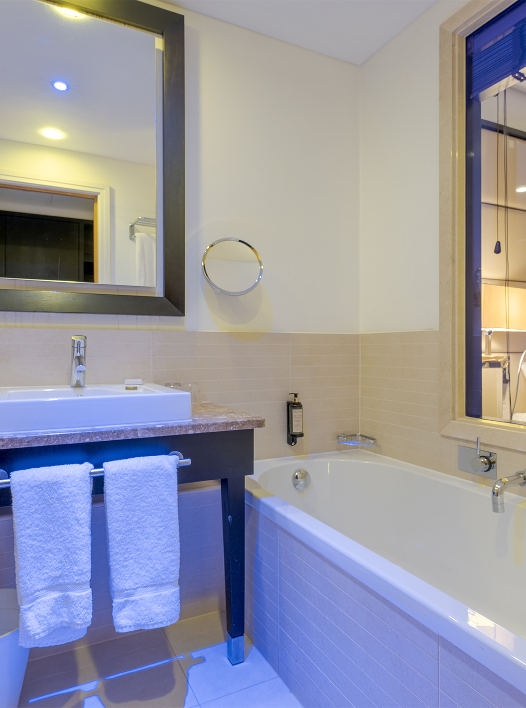 The Twin Deluxe at Pestana Chelsea Bridge has a bathroom with a bathtub, glass to the room, sink, mirrors, and hairdryer