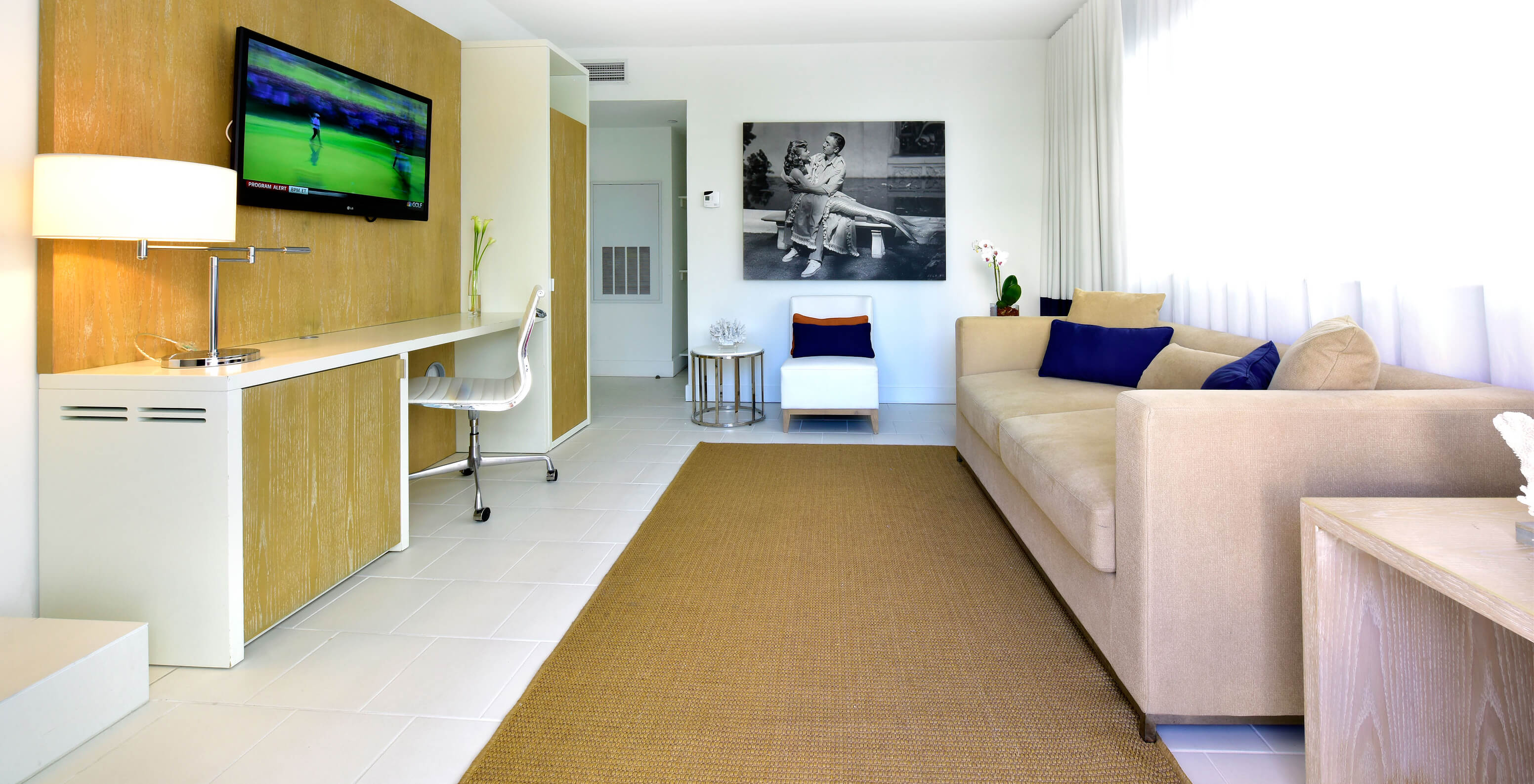 The Two Bedroom Suite with Balcony at Pestana Miami South Beach has a living room with sofa, chair, TV and a desk