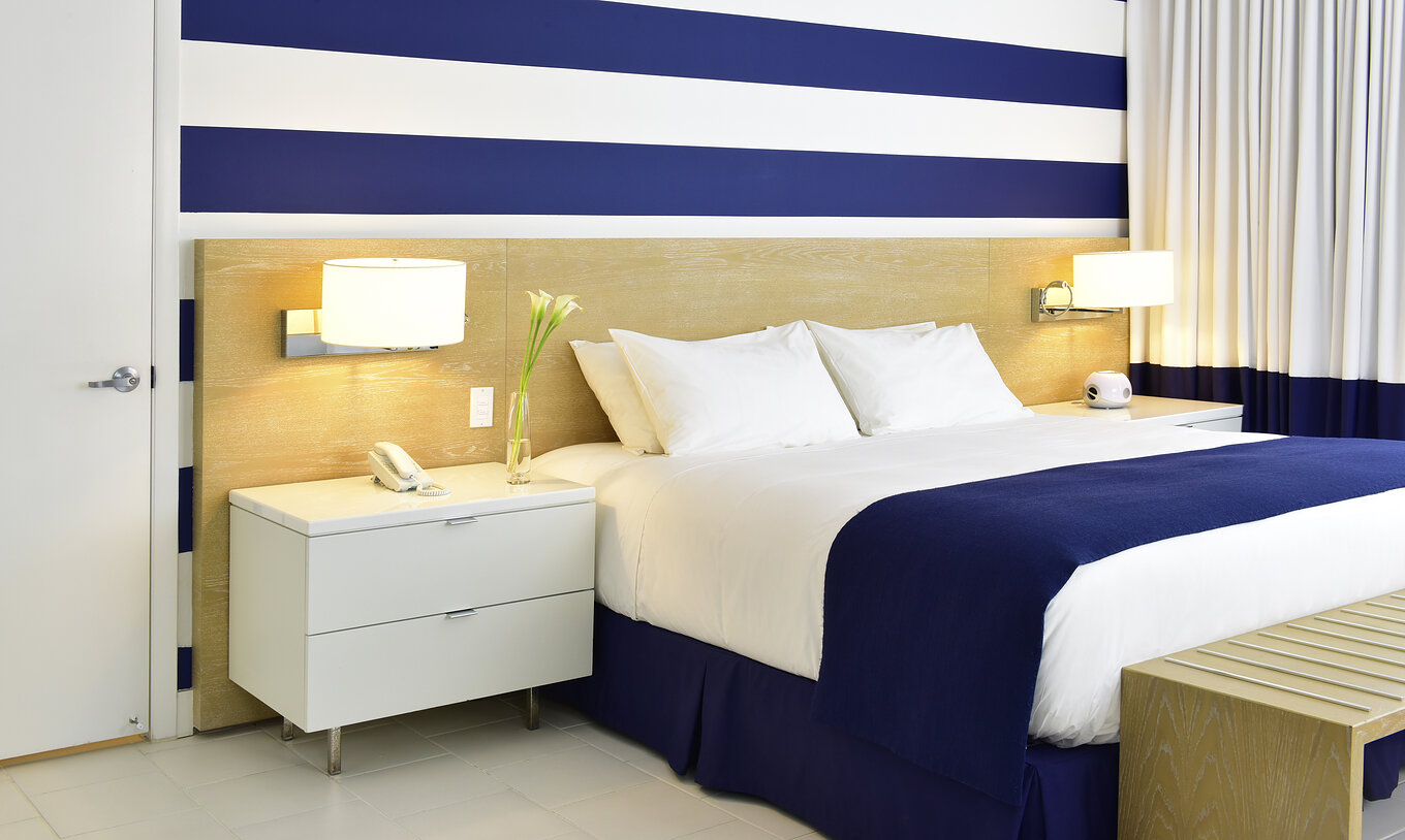 The Pestana Deluxe King Bed Room at Pestana Miami South Beach has a king size bed, lamp and bedside table