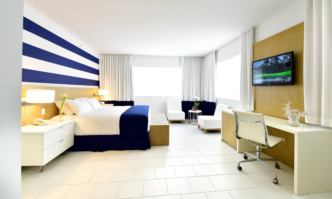 The Pestana Deluxe King Bed Room at Pestana Miami South Beach has a king size bed, lamp, table and two chairs