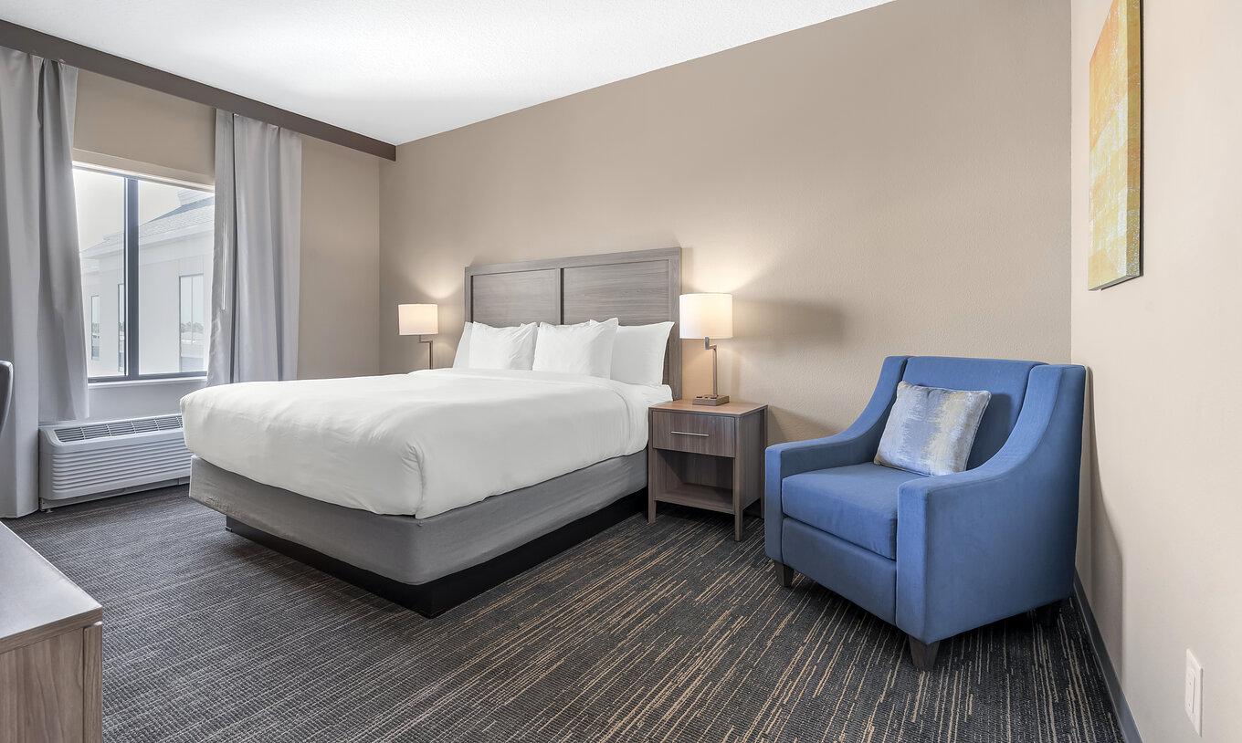 The King Room at Pestana Orlando Suites Lake Buena Vista has a double bed, a bedside table, and an armchair