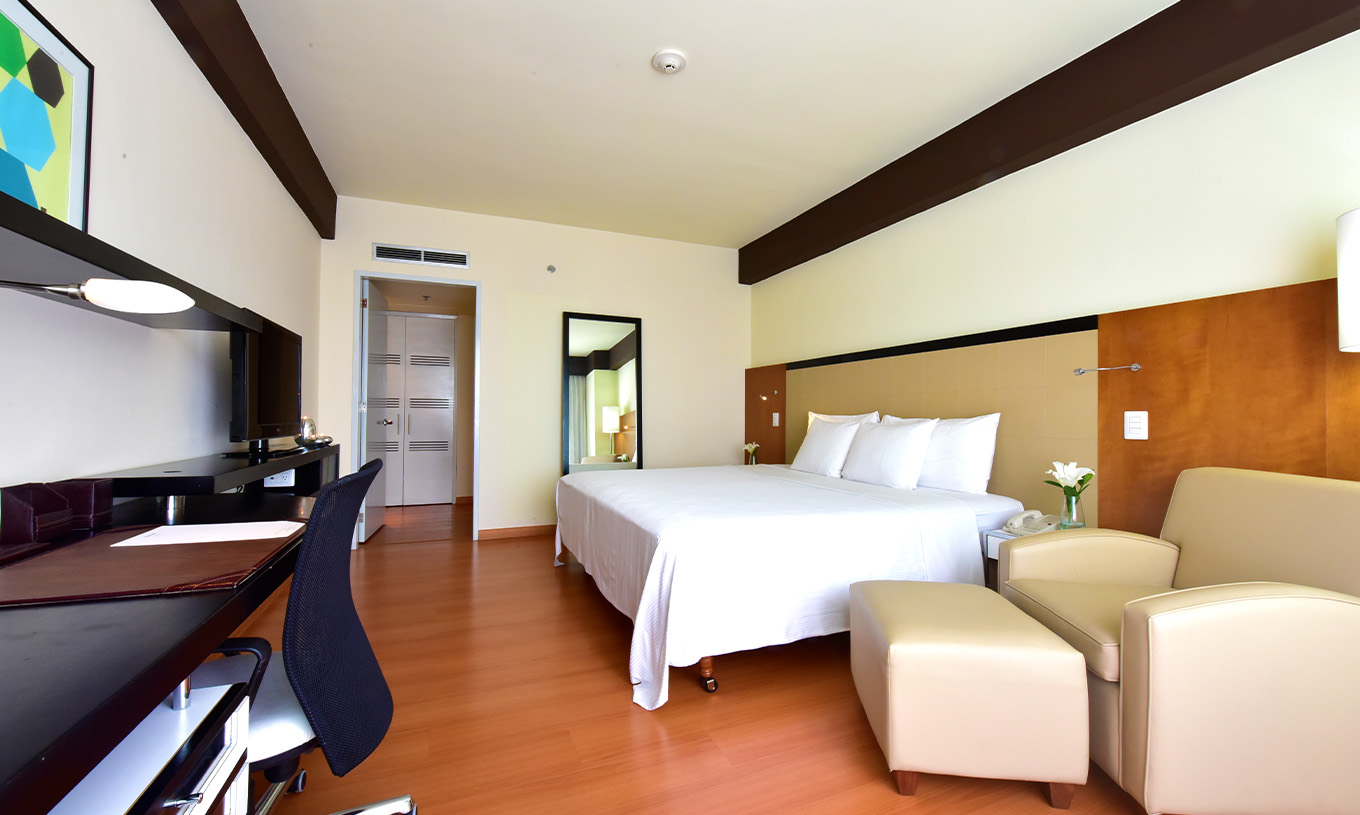 The Executive King Room at Pestana Caracas has a double bed, a large mirror, a desk, and an armchair