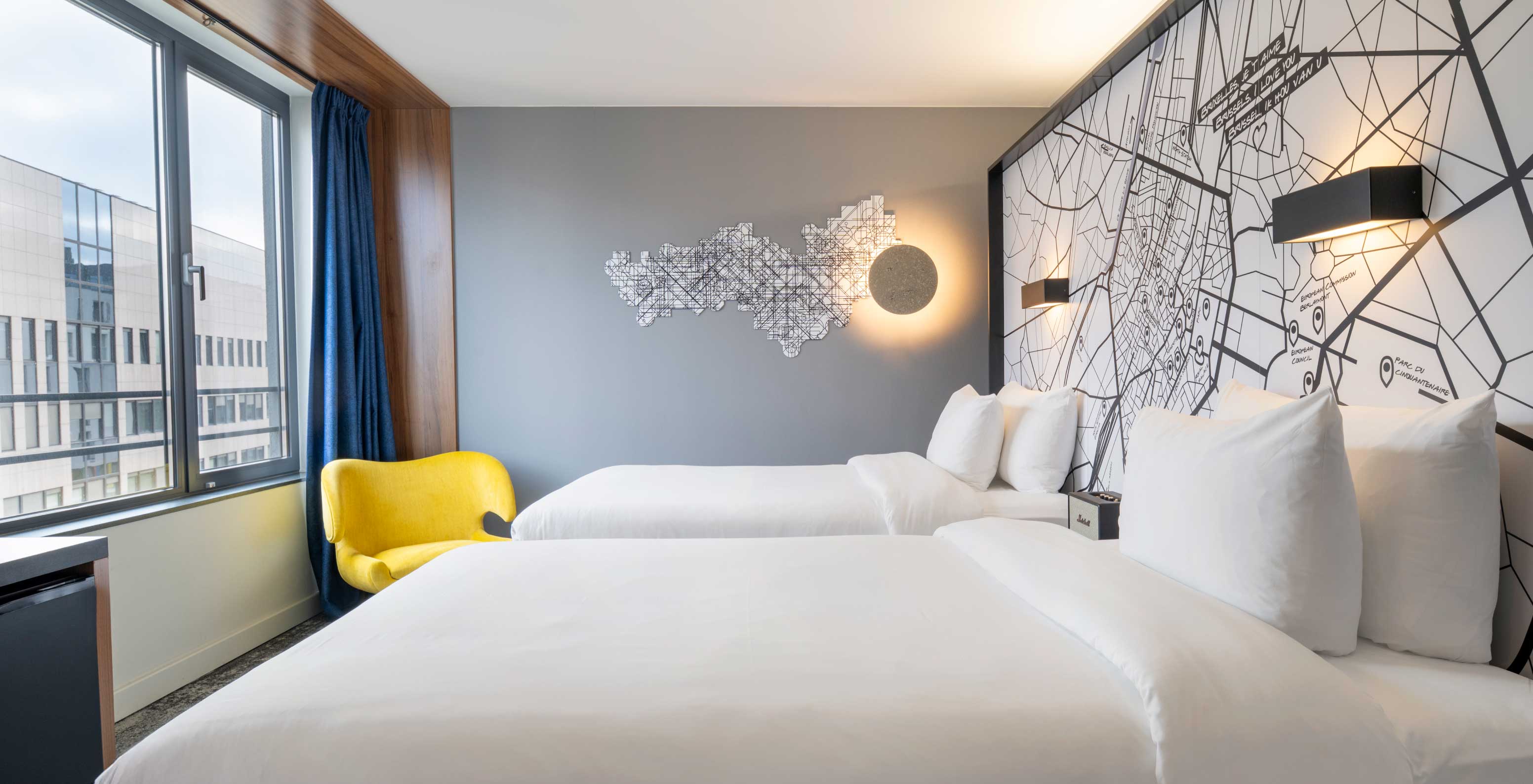 The Superior Twin at Pestana Brussels Schuman has two single beds, a yellow chair, and a window with a view