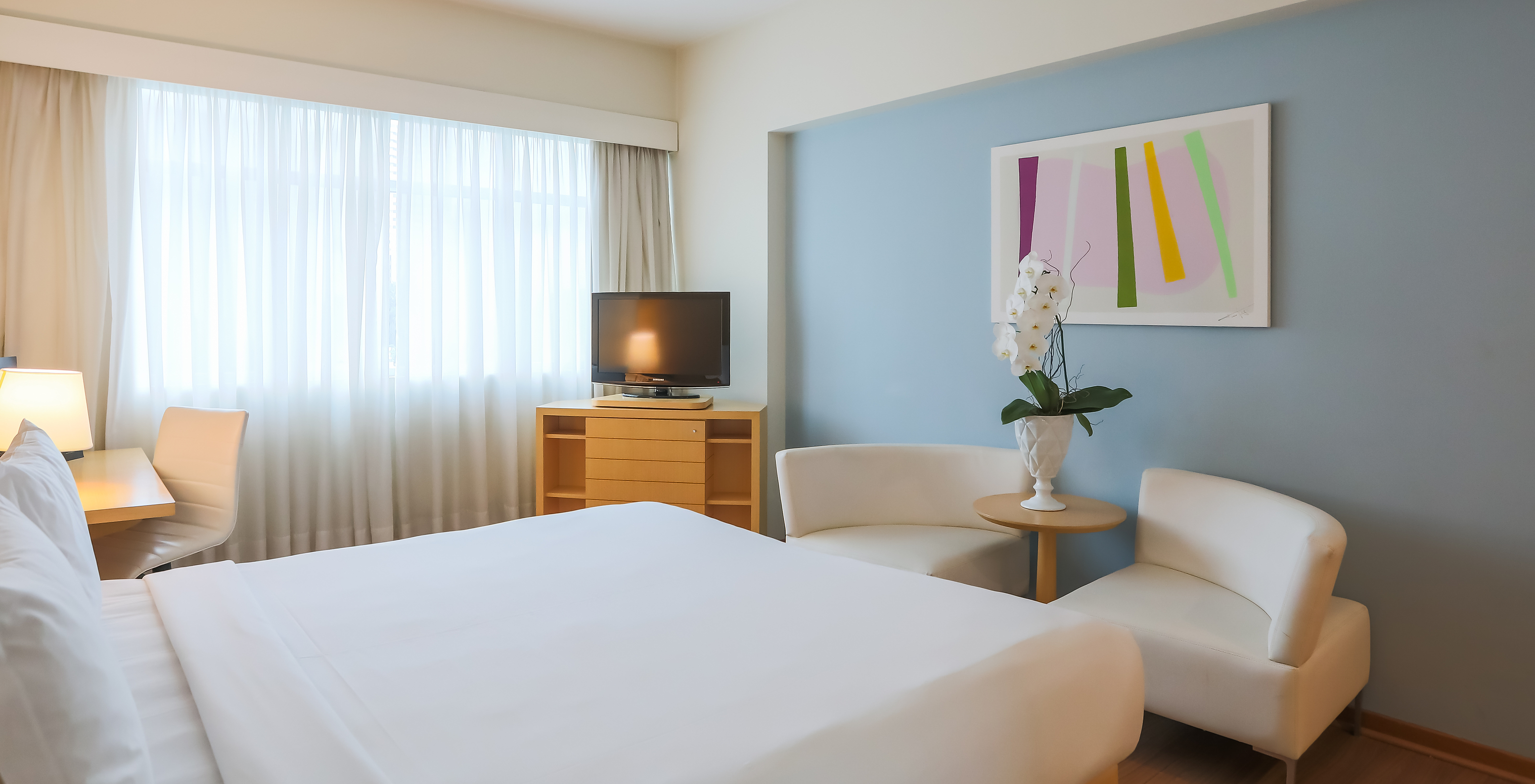 The Queen Luxury Corner at Pestana Curitiba has a double bed, two sofas, a furniture unit with a TV, and a desk