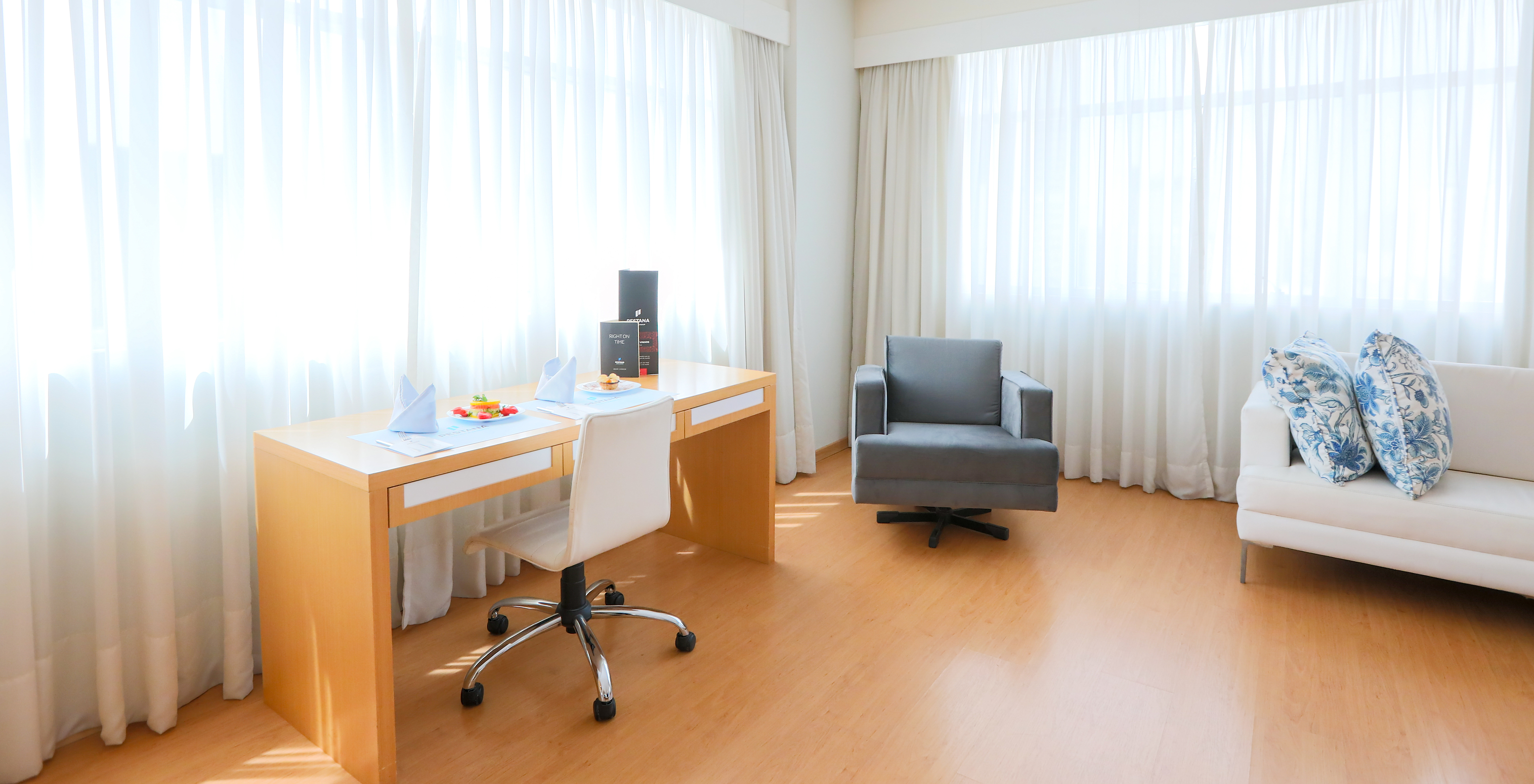 The Queen Luxury Corner at Pestana Curitiba has sofas and a desk next to two large windows that let in plenty of light