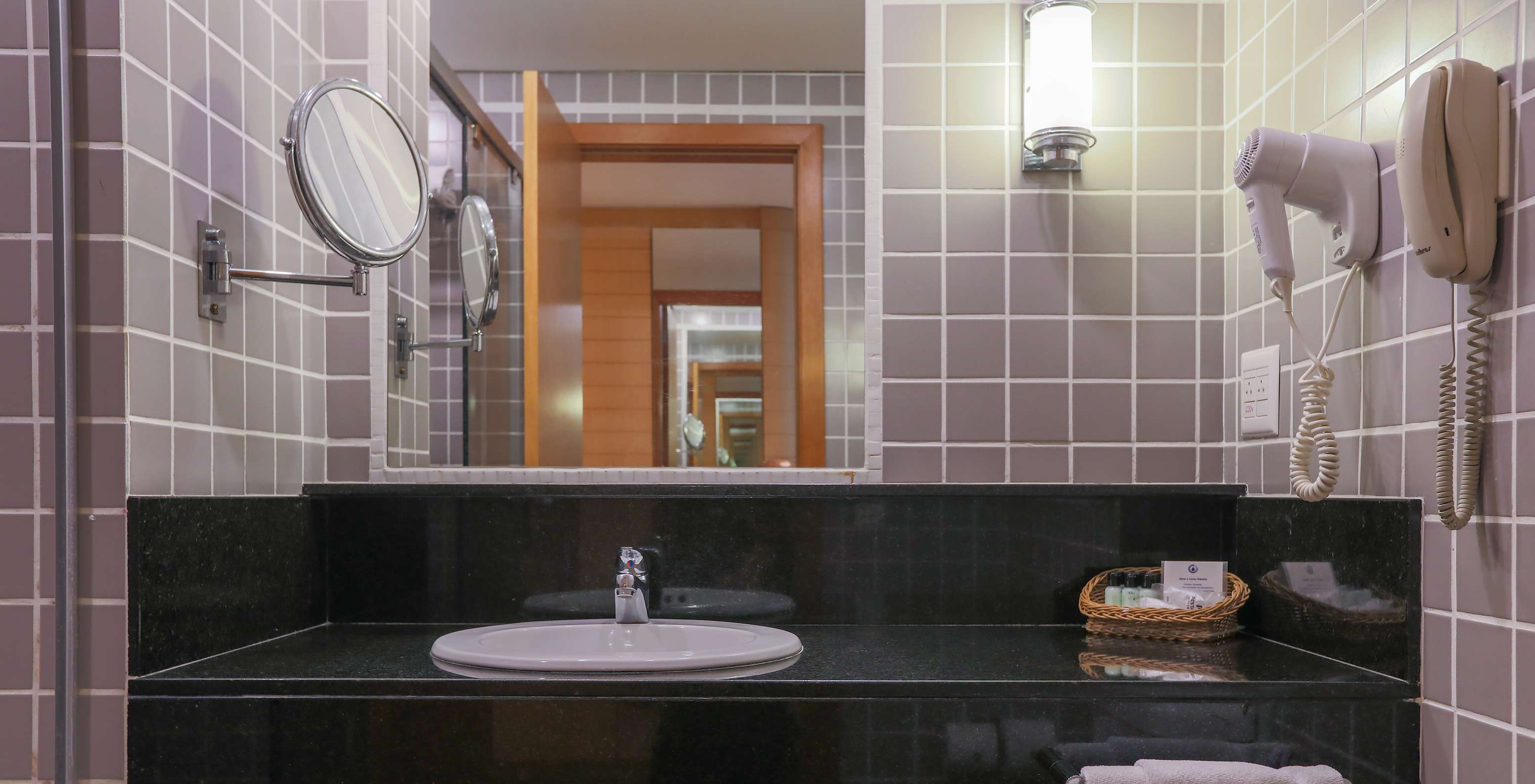 The Deluxe Corner at Pestana Curitiba has a bathroom with gray tiles and a black countertop with a sink