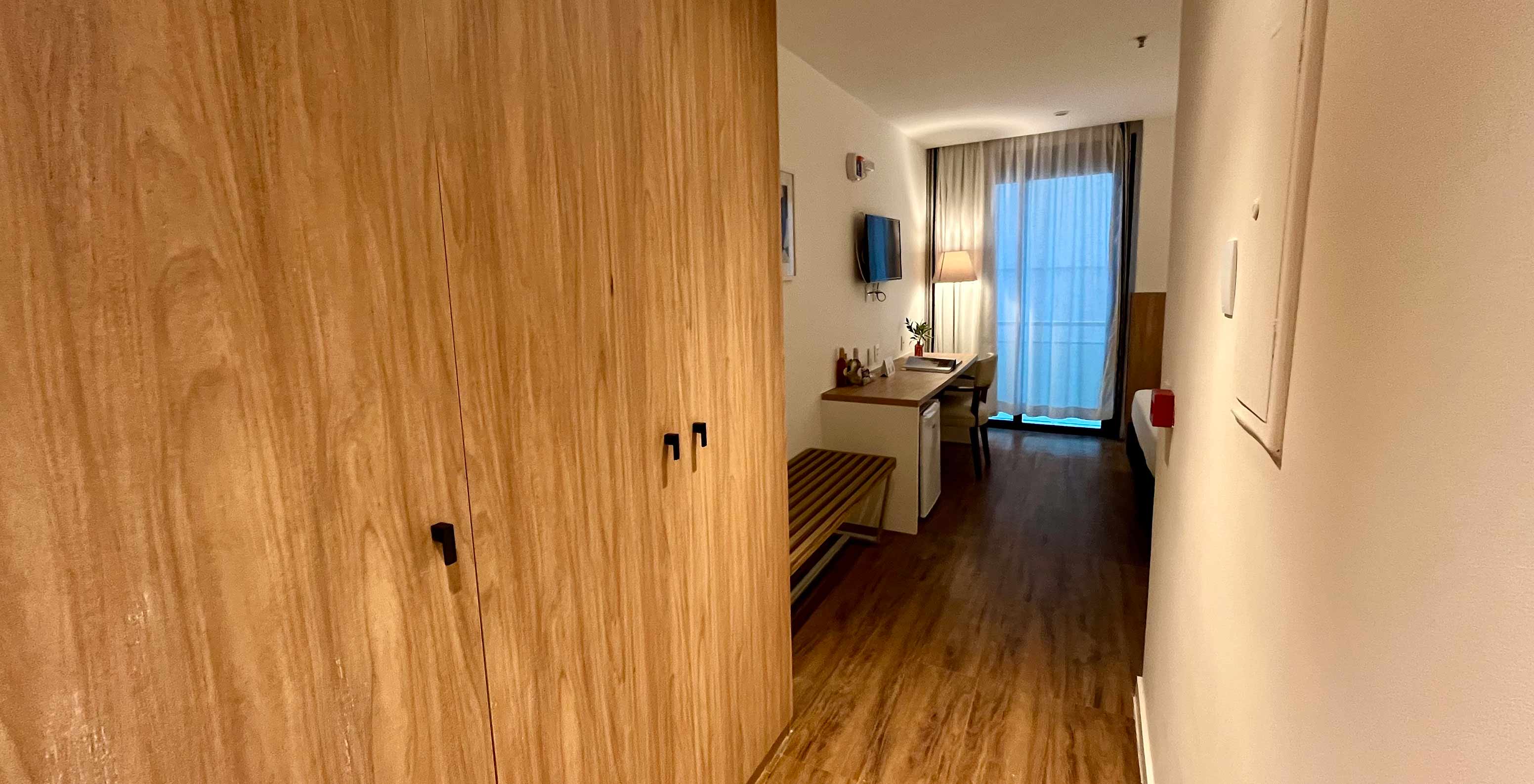 The Semi-Adapted Room at Pestana Rio Atlântica has a hallway with wooden wardrobe and desk by the window