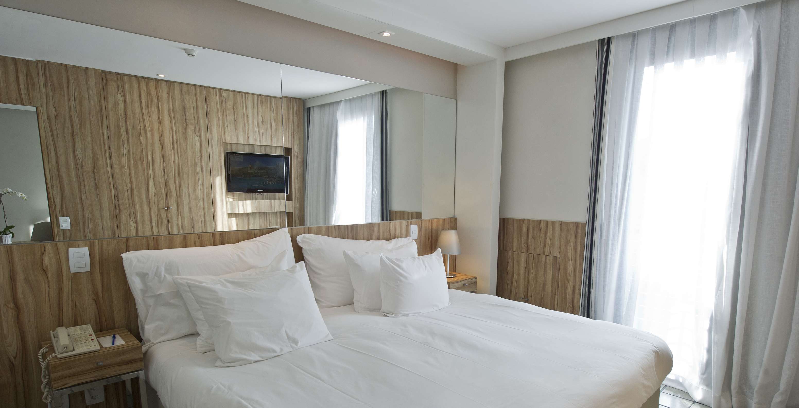 The Suite Standard of Pestana Rio Atlântica has a double bed with a mirror on the headboard and two nightstands