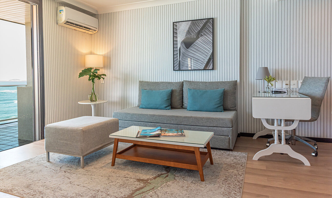 The Oceanic Suite at Pestana Rio Atlântica has a modern lounge with sofa, desk, table and sea view.