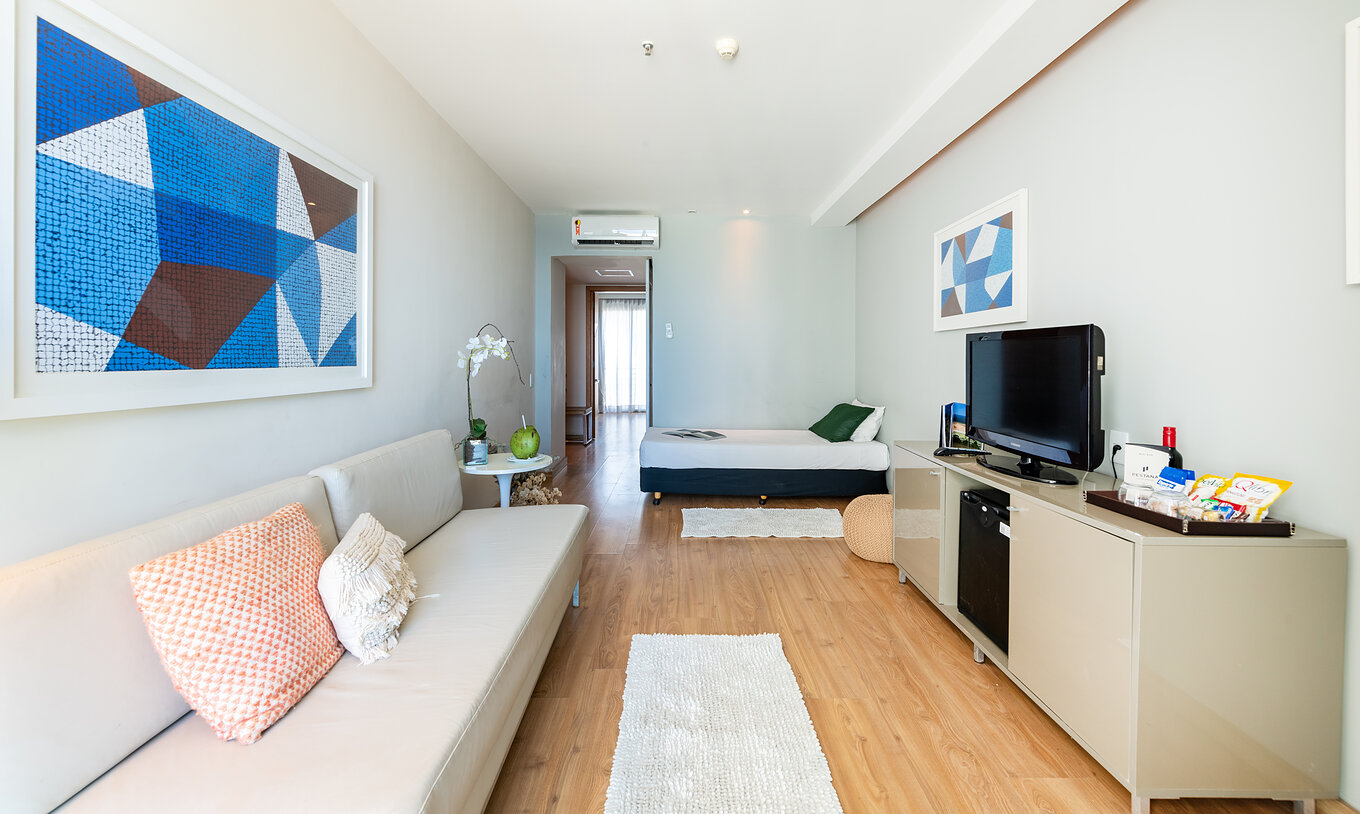 The Lateral Sea View Suite of Pestana Rio Atlântica has a living room with a sofa, single bed, television and a blue painting