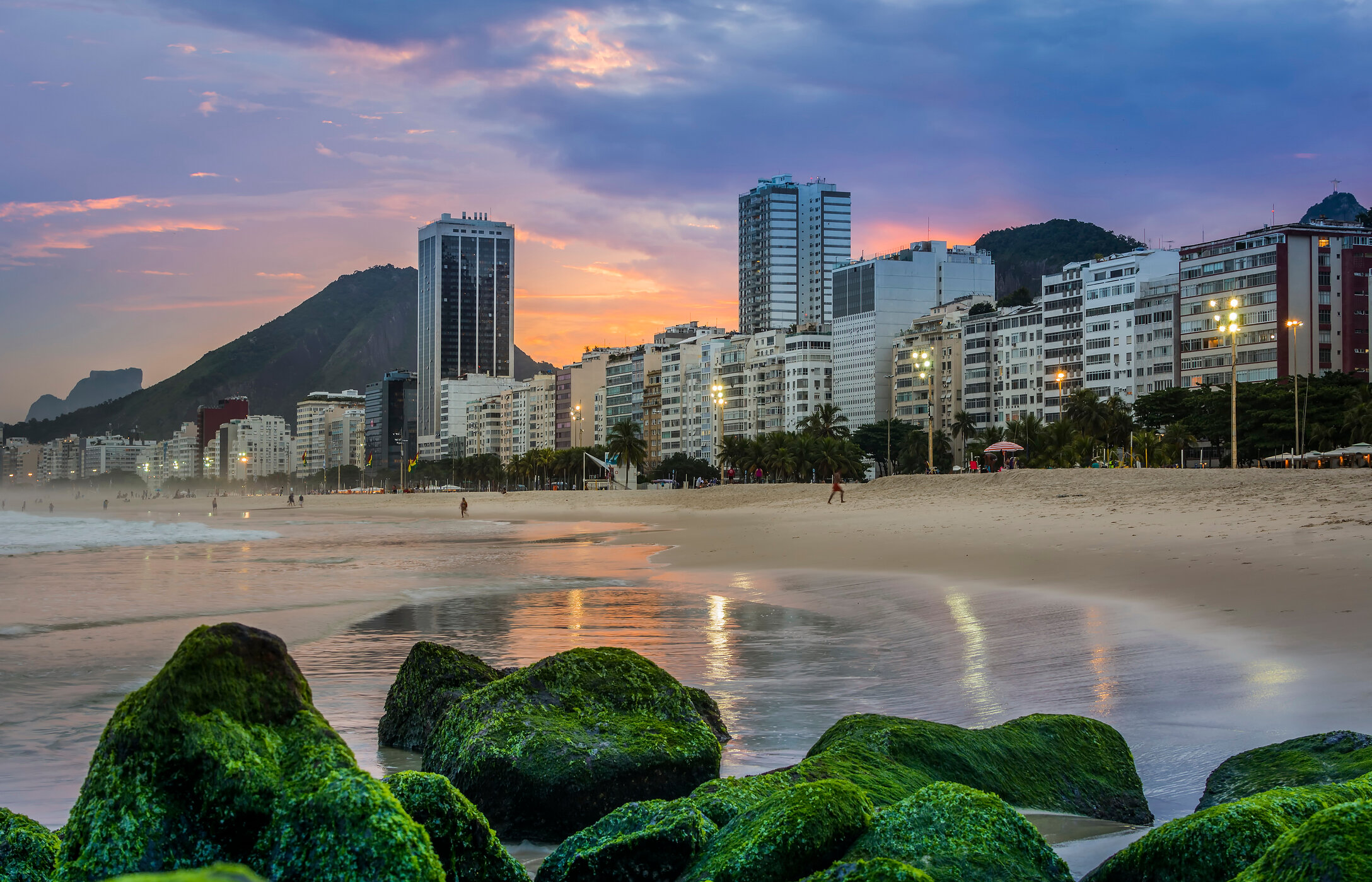 Copacabana Beach, with golden sands, sea waves, and a busy promenade, surrounded by buildings and mountains in the background