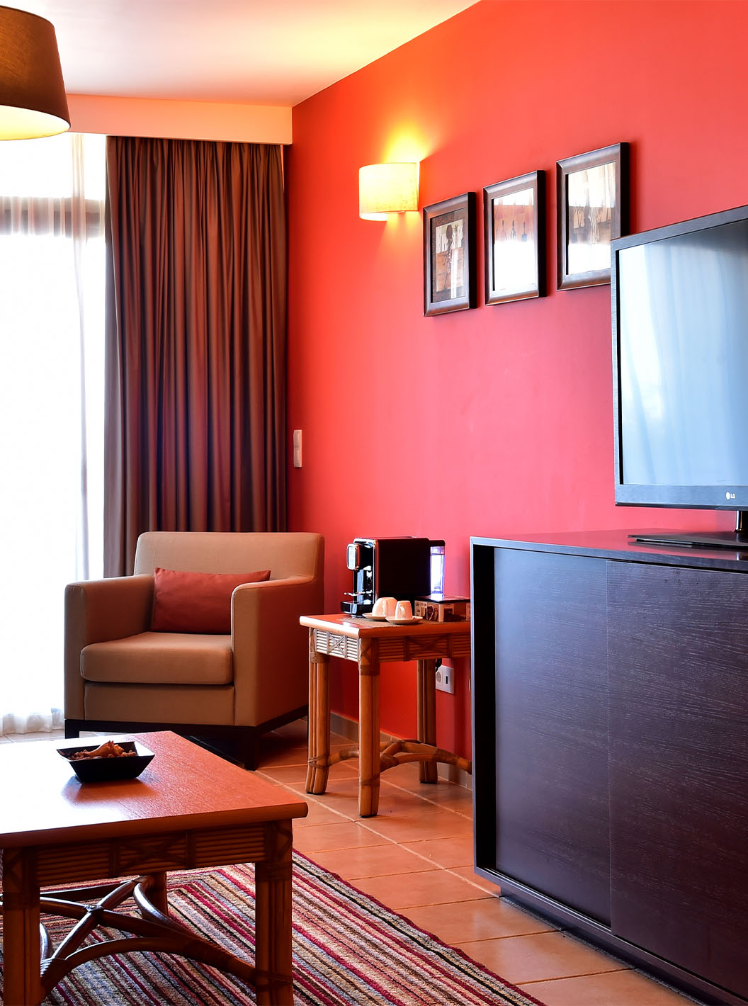 The Suite at Pestana Tropico features a living room with dining table, armchair, coffee table, and a television