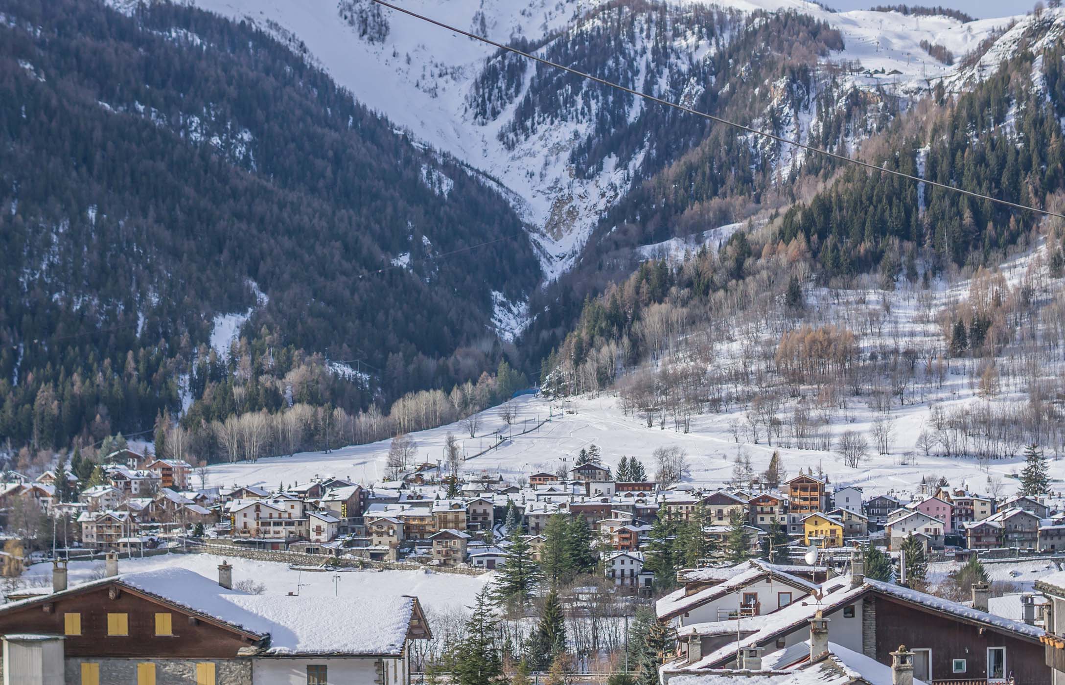 Snow covered mountain village with alpine houses, forested slopes and ski lines across the valley in winter