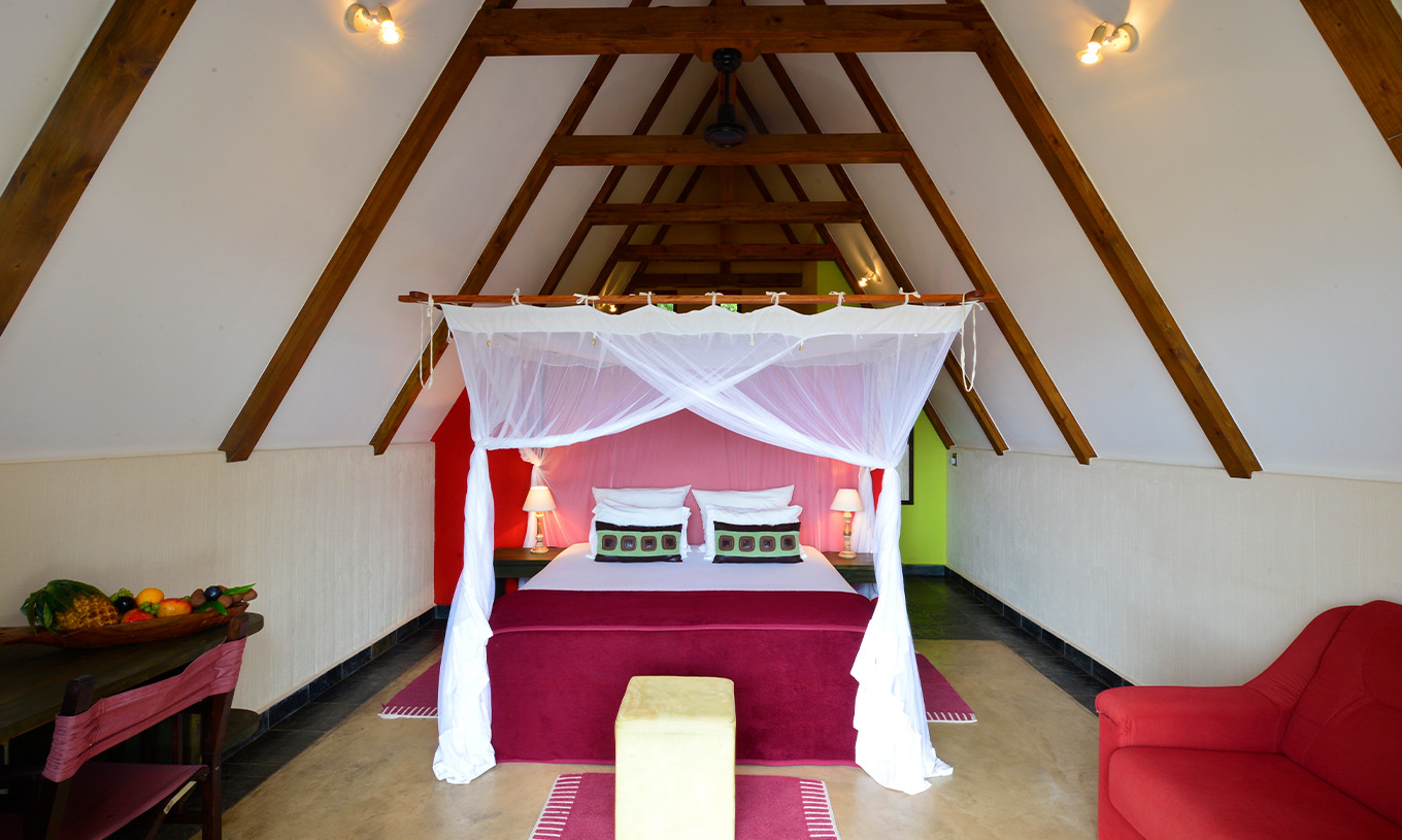 Bungalow T1 at Pestana Bazaruto Lodge has a double bed with canopy, a sofa and a desk with a bowl of fruit