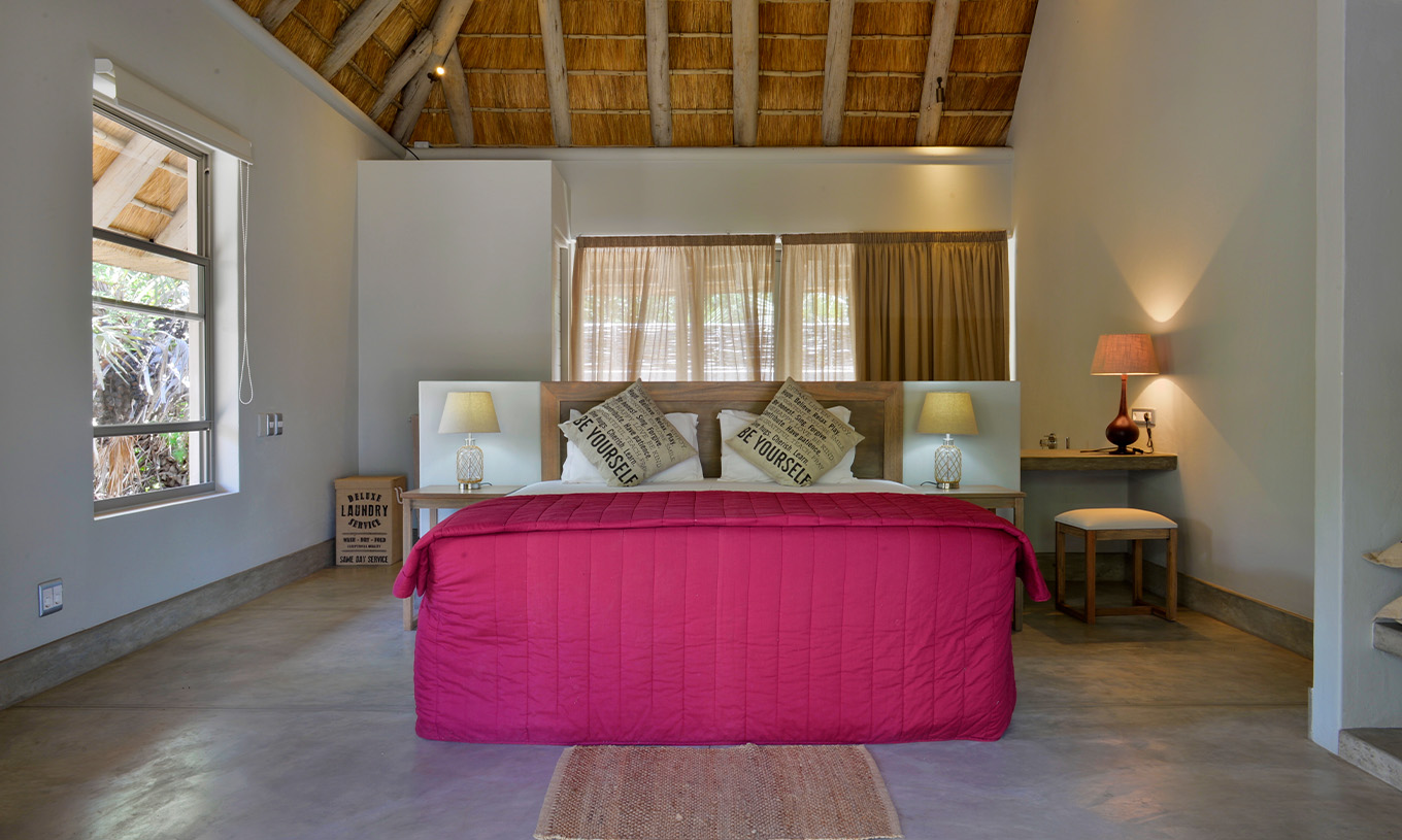 T2 Villas at Pestana Bazaruto Lodge are quite spacious with a double bed with red bedspread and windows around