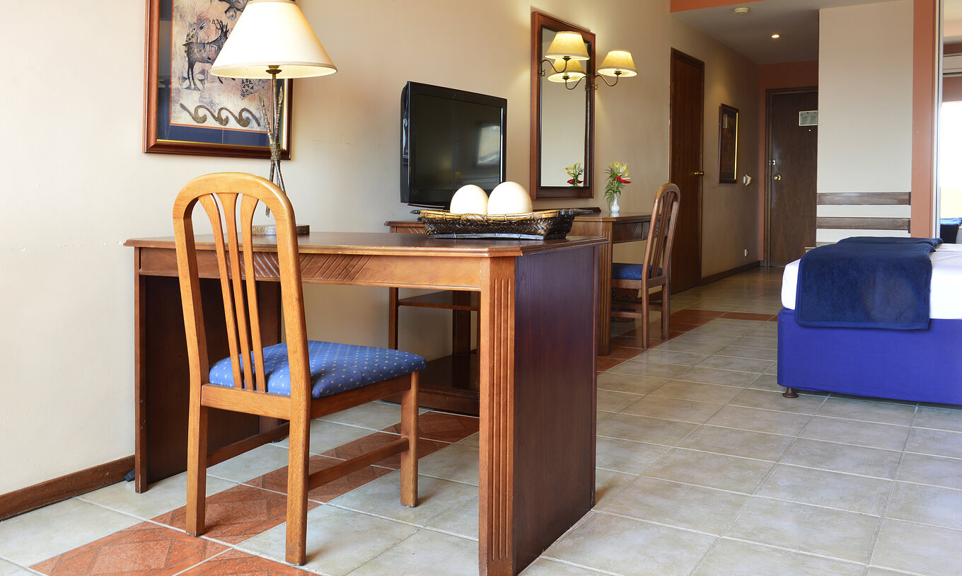 The Family Executive Suite of Pestana Rovuma has a desk and wooden chair, with a lamp and a picture