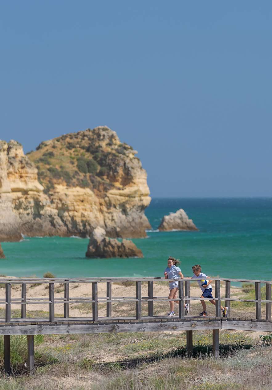 Children running along the Alvor walkway near Pestana Dom João II, Hotel 4 Estrelas no Algarve with coastal cliffs