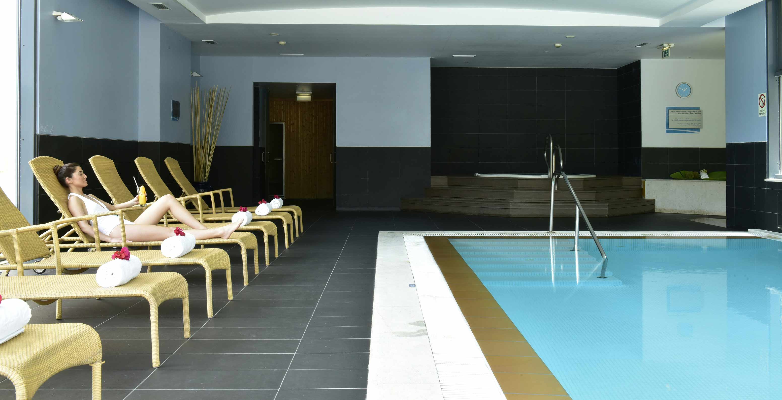 Guest relaxing on sun loungers by the indoor pool at Pestana Alvor Park, a 4-star Aparthotel in Alvor with a swimming pool