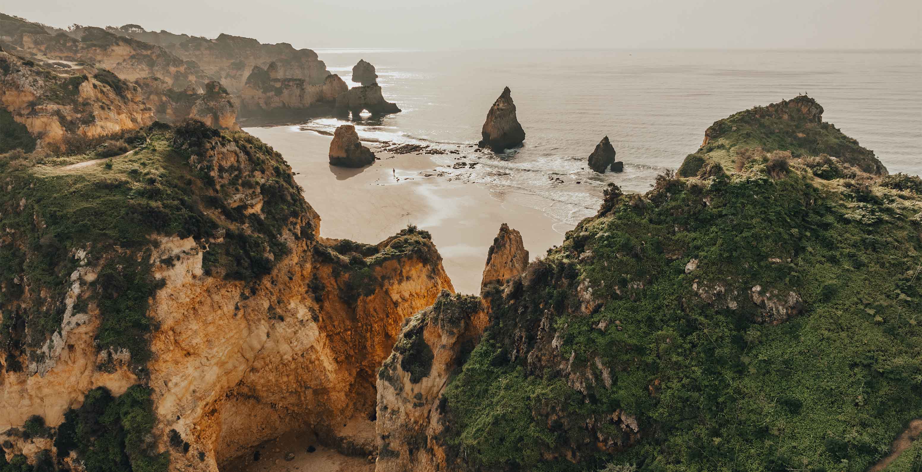 Aerial view of Três Irmãos Beach with rock formations, vegetation, sea fog in background