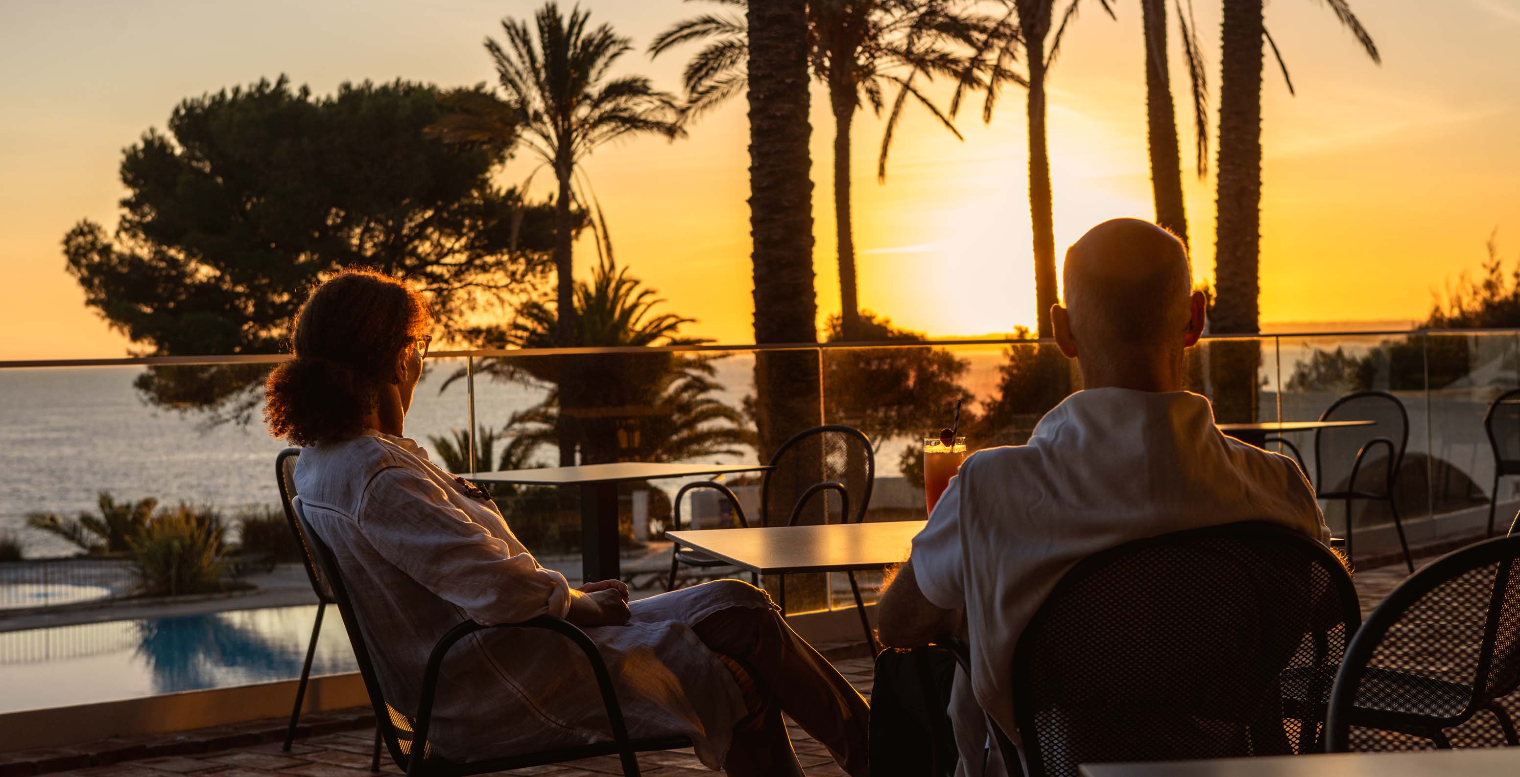 Couple enjoying the sunset with a view of the pool, sea, and palm trees at Pestana Alvor Praia