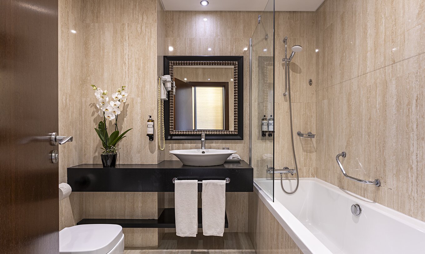 The Cliff Family at Pestana Alvor Praia has a modern bathroom with a bathtub, a sink, a toilet, a mirror, and flowers