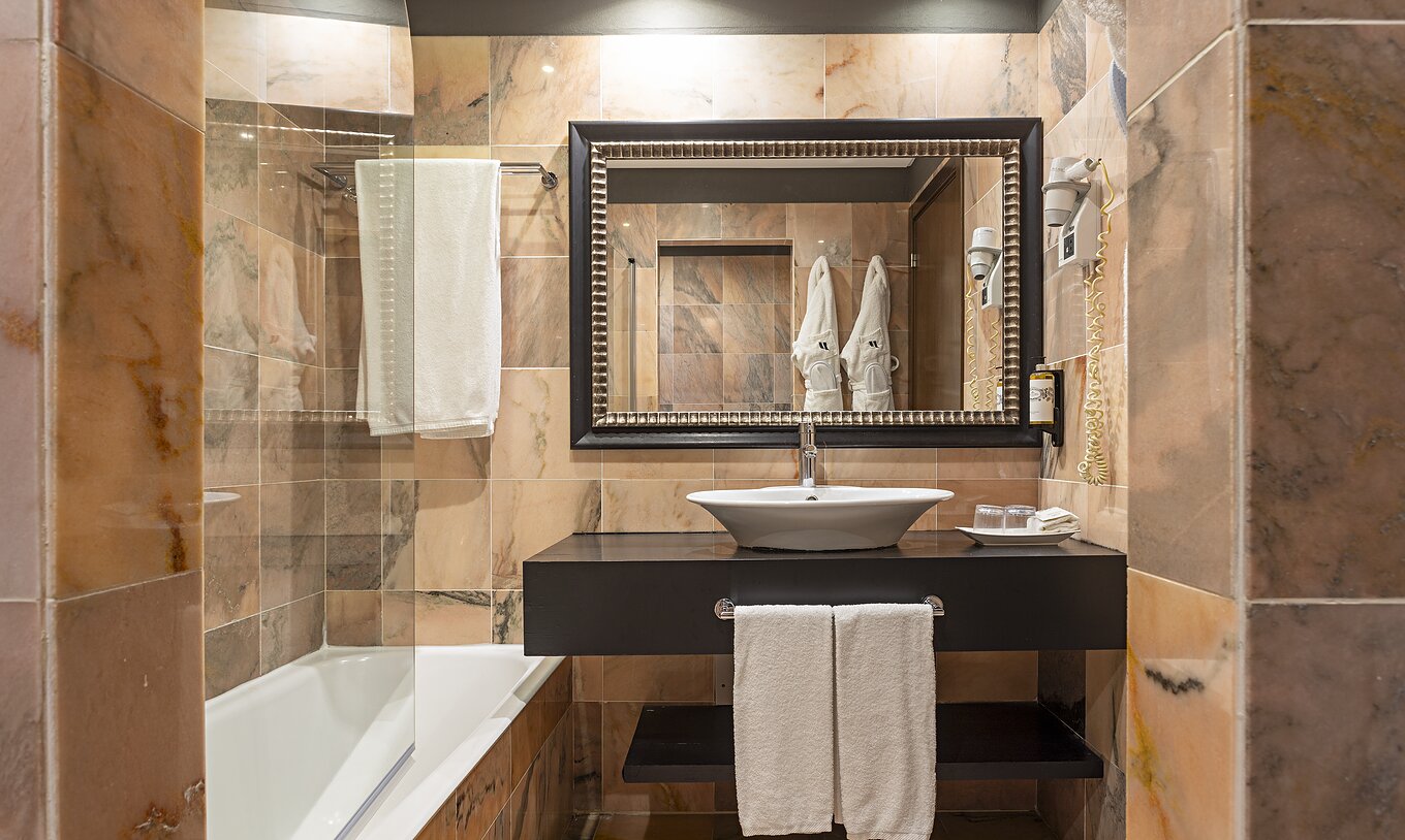 The Cliff Suite T1 at Pestana Alvor Praia has a bathroom with a bathtub, two bathrobes, and a hairdryer