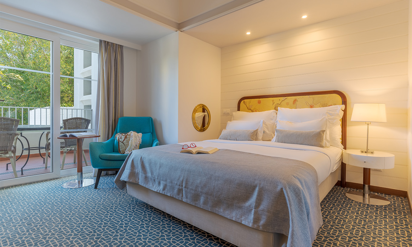The Garden View Deluxe at Pestana Alvor Praia has a double bed, a blue armchair, and a window to the balcony