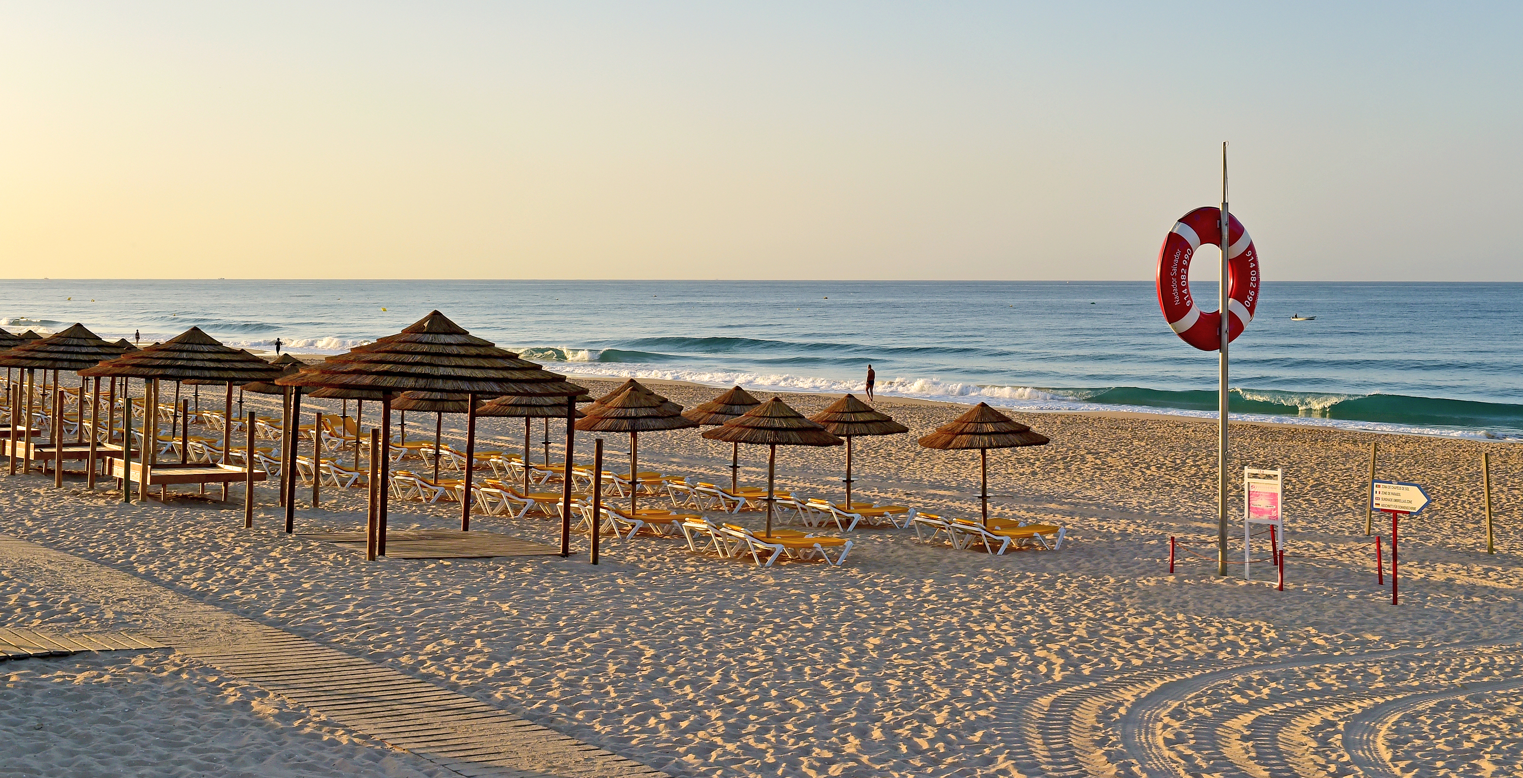 Thatch huts with loungers on Alvor Beach, light sand, calm waves, peaceful setting
