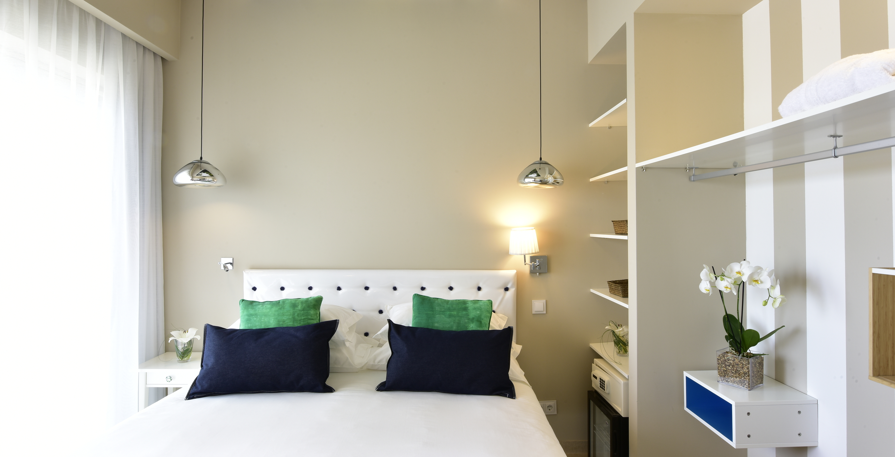 The Suite of Pestana Alvor South Beach has a double bed with a window on one side and an open wardrobe with minibar