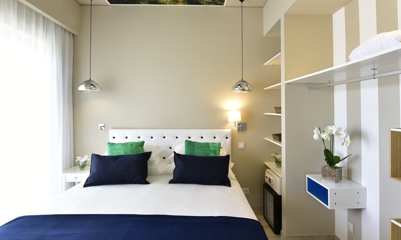 The Suite of Pestana Alvor South Beach has a double bed with a window on one side and an open wardrobe with minibar