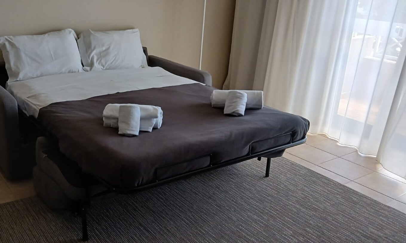 The studio at Pestana Gramacho Residences has an open sofa bed with white sheets and folded towels