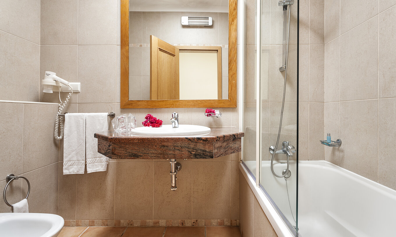 The T1 Apartment Land do Pestana Palm Gardens has a bathtub with shower, a sink with flowers and a mirror