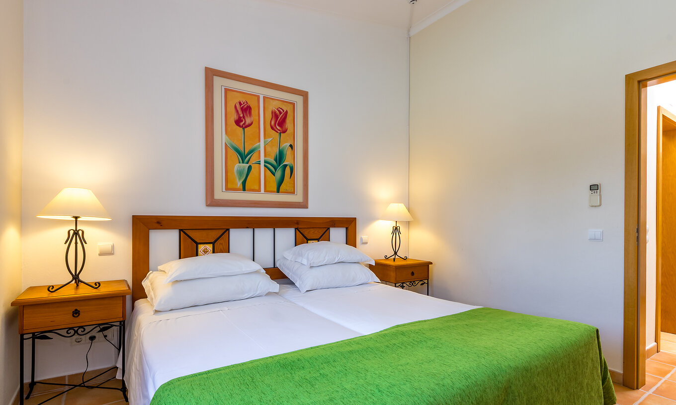 The T1 Apartment Land do Pestana Palm Gardens has two beds together, with a green bedspread and a painting with flowers