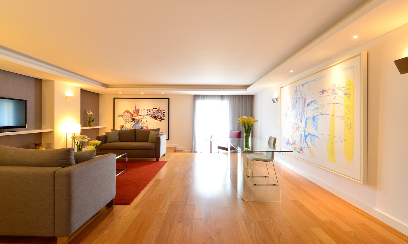 The Presidential Suite at Pestana Cidadela Cascais has a living room with a transparent desk and chair, paintings, and a sofa