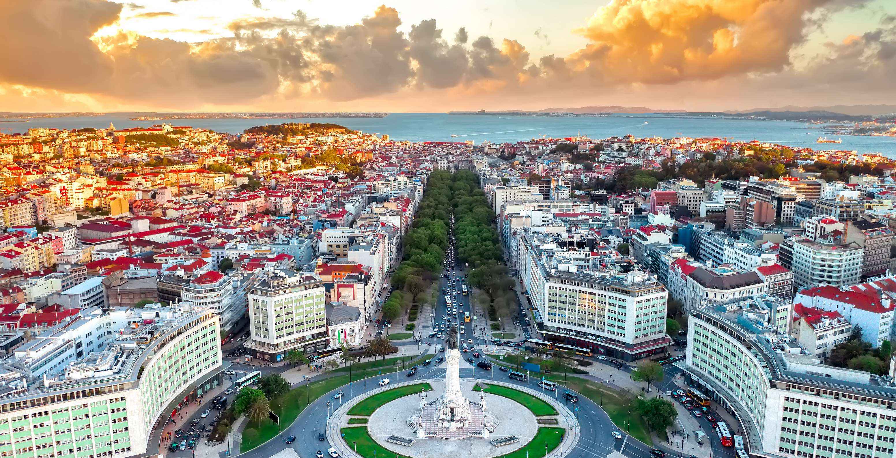 Aerial view of Marquês de Pombal roundabout with buildings, cars, trees, the Tagus River in the background